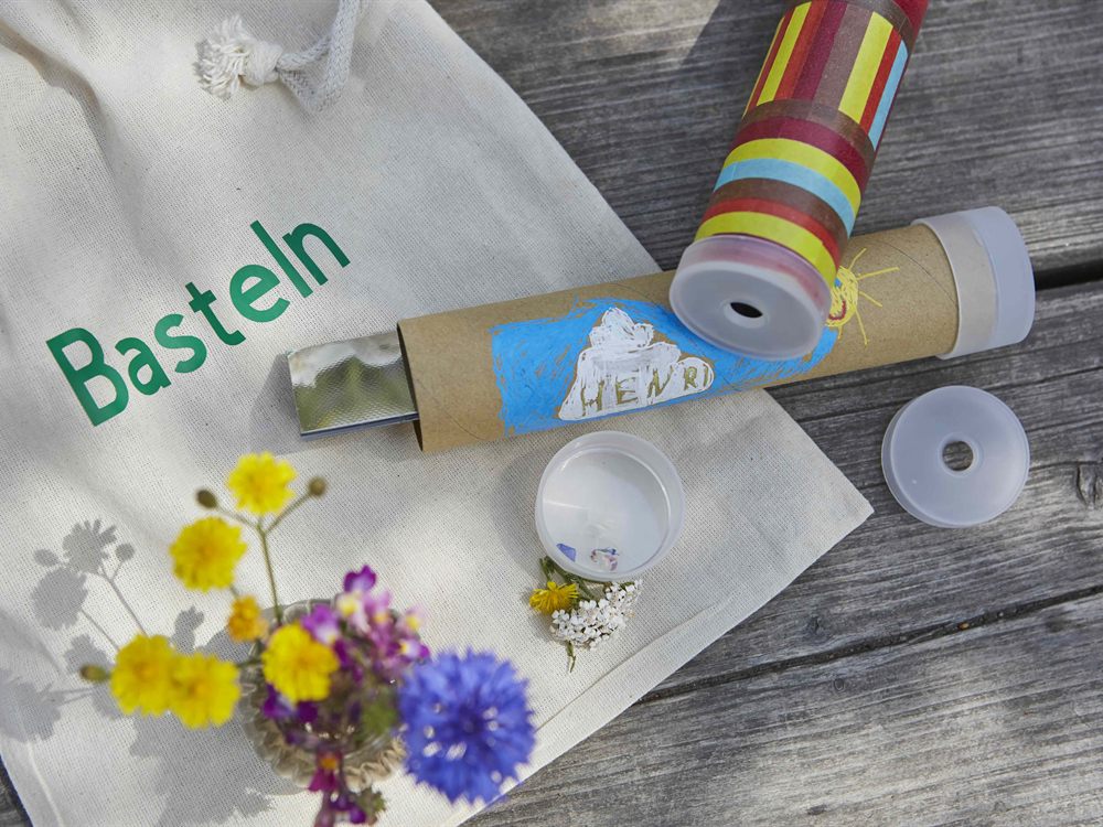 Selbst gestaltetes Kaleidoskop aus Pappe mit Washi-Tape, daneben gesammelte Wiesenblueten